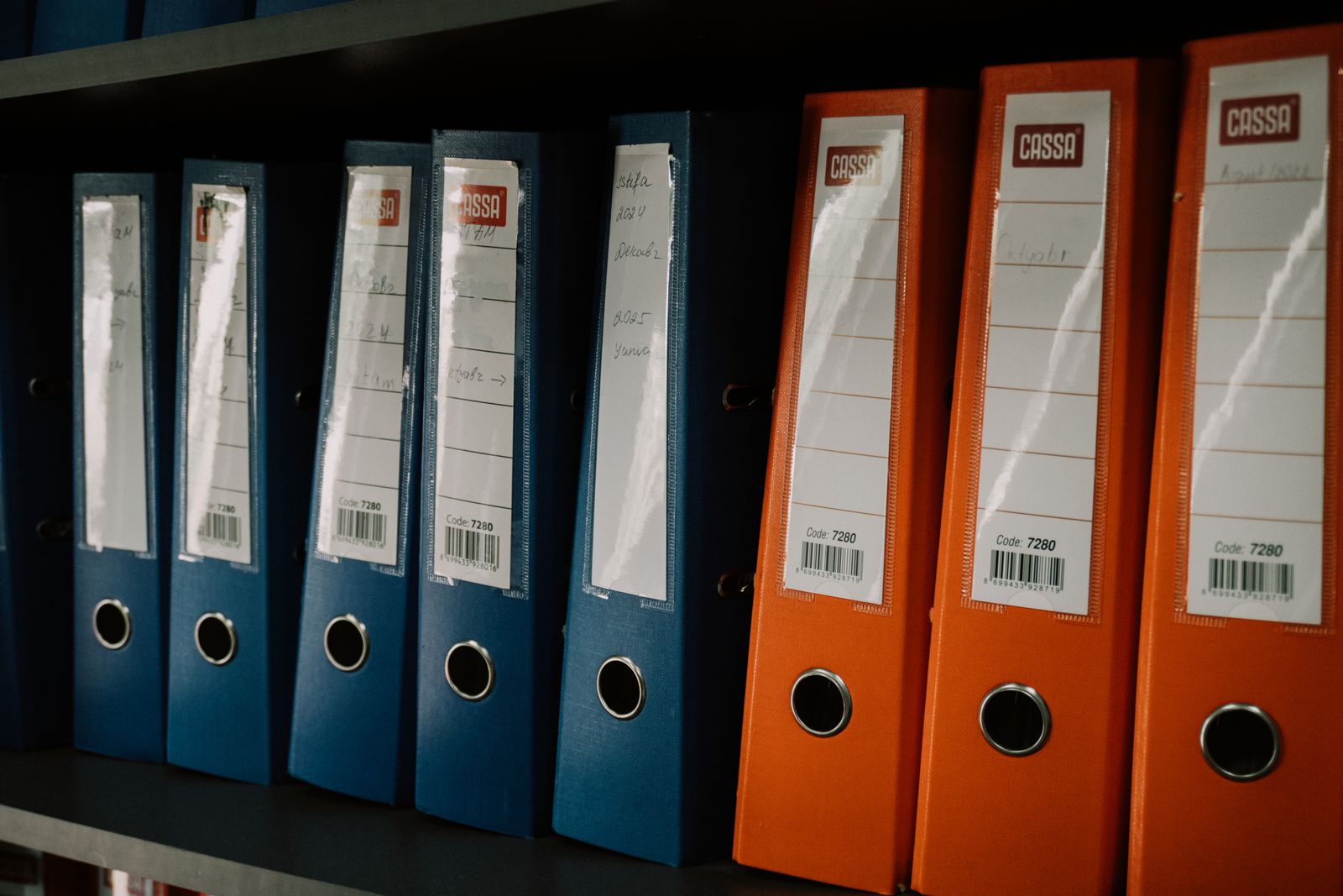 Two sets of labeled binders, one blue and one orange, filed on the same shelf